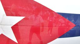 ARCHIVO - Niños caminan a través de la bandera cubana hacia el Malecón habanero para lanzar flores al mar en conmemoración del aniversario de la muerte del Comandante revolucionario cubano Camilo Cienfuegos, el jueves 28 de octubre de 2004 en La Habana, Cuba. (Foto AP/Cristóbal Herrera, Archivo)