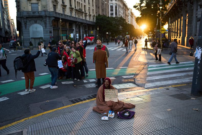 ARCHIVO - Patricio Roblez, sosteniendo un cartel con un mensaje en español que dice que no tiene hogar, pide limosna mientras los manifestantes posan para una selfie grupal en Buenos Aires, Argentina, el 11 de junio de 2025. (AP Foto/Rodrigo Abd, Archivo)