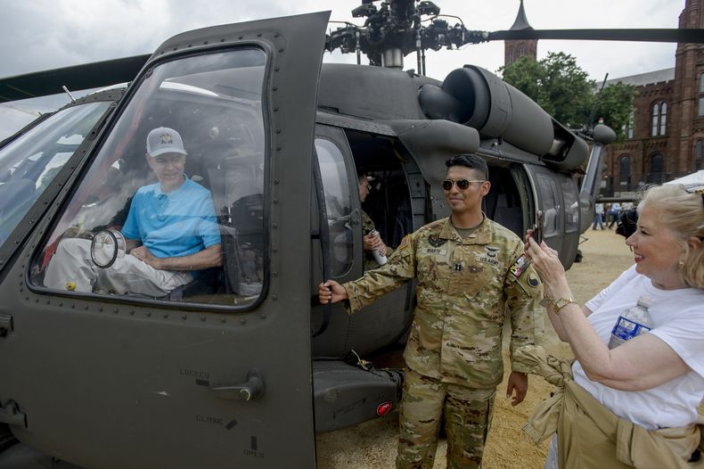 Dale Booth, izquierda, de Tyler, Texas, posa en un helicóptero Blackhawk para su esposa, Jan Booth, derecha, en el festival en honor del 250 aniversario del Ejército de Estados Unidos, que coincide con el 79no cumpleaños del presidente Donald Trump, el sábado 14 de junio de 2025, en el National Mall de Washington. (AP Foto/Rod Lamkey, Jr.)