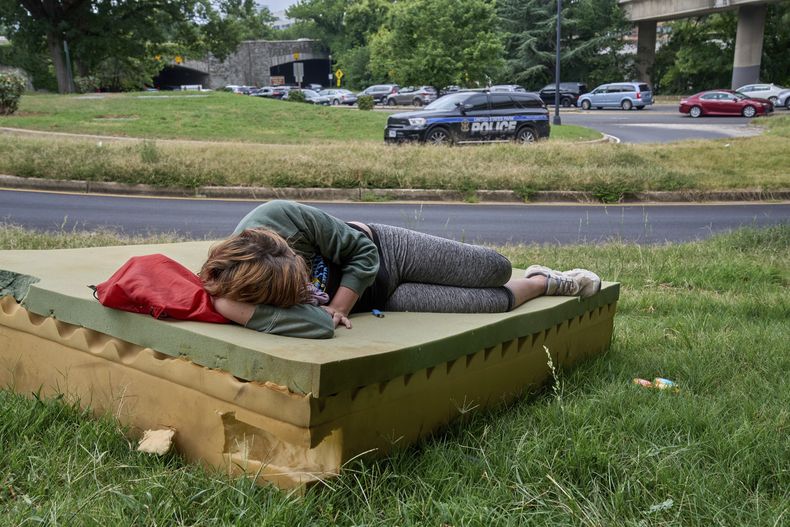 Stephanie W., de 28 años, que no tiene hogar, descansa en un colchón de espuma mientras pasa un vehículo de la Policía de Parques de EEUU, el 13 de agosto de 2025, en el noroeste de Washington, cerca del Kennedy Center. (AP Foto/Jacquelyn Martin)