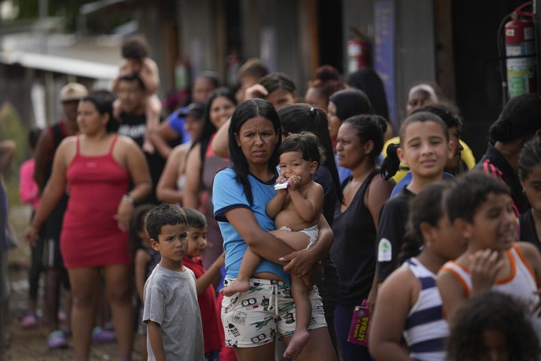 ARCHIVO - La migrante venezolana Minorca Parra sostiene a su hija Karin Alvear mientras hace fila para recibir alimentos en un campamento temporal después de cruzar el Tapón del Darién desde Colombia en Lajas Blancas, Panamá, el 27 de junio de 2024. La migración a través del Tapón del Darién que divide a Colombia y Panamá ha disminuido significativamente este mes desde que el presidente panameño José Raúl Mulino asumió el cargo y ordenó a las autoridades tomar el control de la densa selva fronteriza, dijo la policía fronteriza del país el miércoles 17 de julio de 2024. (AP Foto/Matías Delacroix, Archivo)