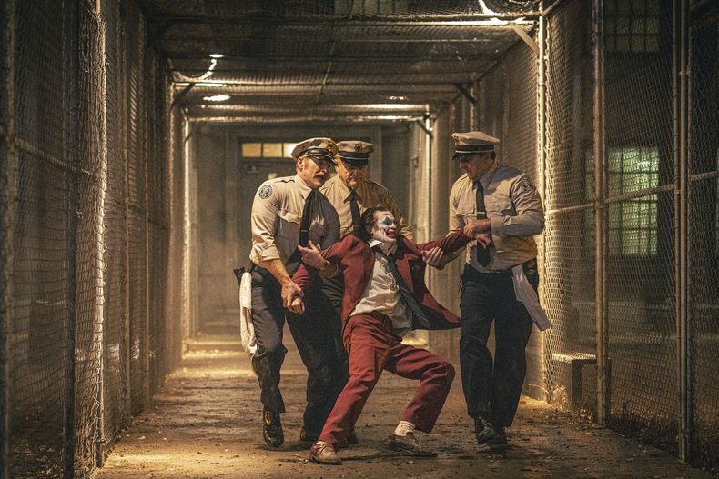 Esta imagen proporcionada por Warner Bros. Pictures muestra a Joaquin Phoenix, en primer plano al centro, y Brendan Gleeson, al fondo en el centro, en una escena de Joker: Folie à Deux. (Niko Tavernise/Warner Bros. Pictures vía AP)