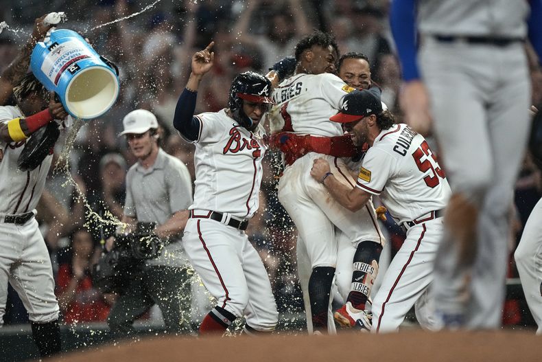 Ozzie Albies (centro) es felicitado por sus compañeros tras empujar la carrera del triunfo sobre los Dodgers de Los Ángeles, el miércoles 24 de mayo de 2023 (AP Foto/John Bazemore)