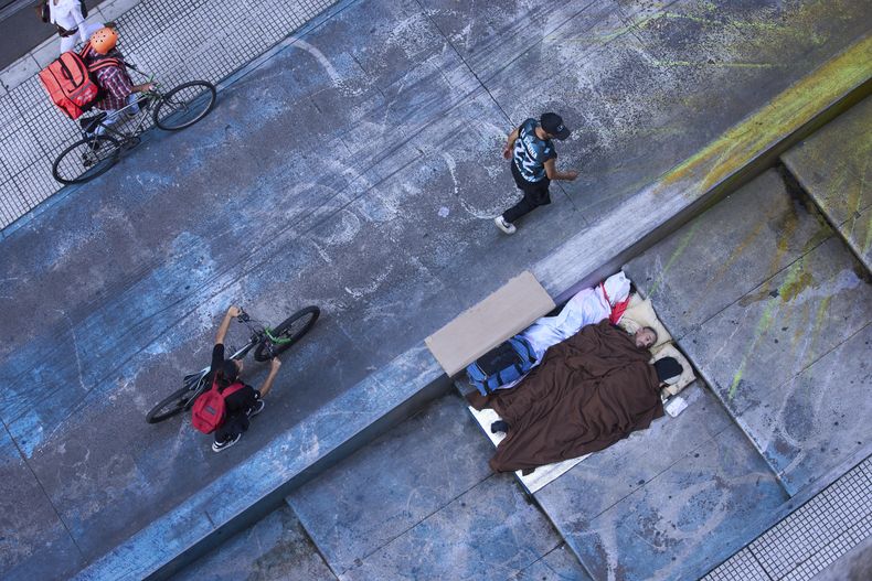 Varias personas pasan al lado de personas durmiendo en la calle en Buenos Aires, Argentina, el viernes 11 de abril de 2025. (AP Foto/Rodrigo Abd)