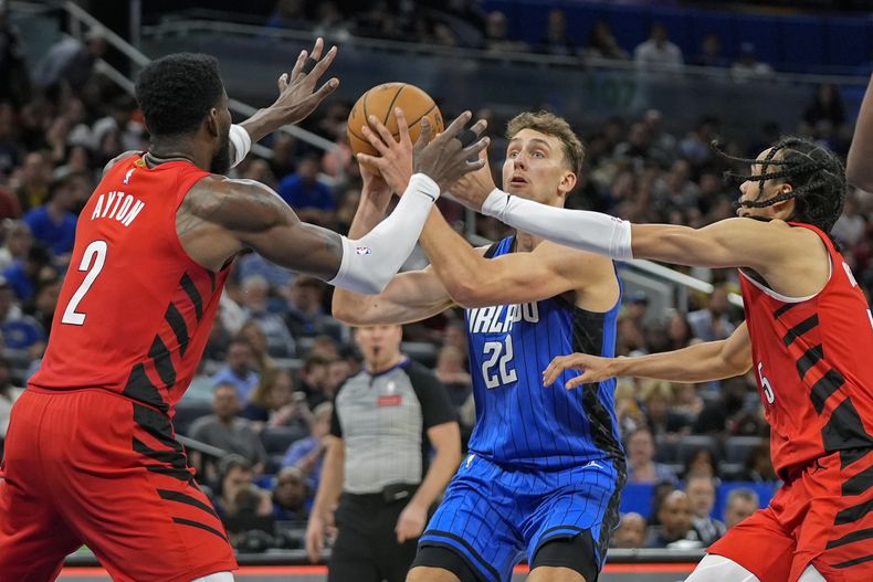 Franz Wagner (22), del Magic de Orlando, busca tomar un tiro ante la doble marca defensiva de Deandre Ayton (2) y Dalano Banton, derecha, de los Trail Blazers de Portland, durante la segunda mitad del juego de baloncesto de la NBA, el lunes 1 de abril de 2024, en Orlando, Florida. (AP Foto/John Raoux)