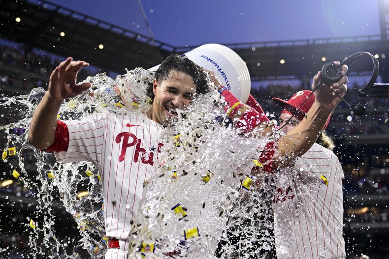 Tyler Phillips, de los Filis de Filadelfia, es empapado por sus compañeros Brandon Marsh y Bryson Stott, tras la victoria del sábado 27 de julio de 2024, ante los Guardianes de Cleveland (AP Foto/Derik Hamilton)
