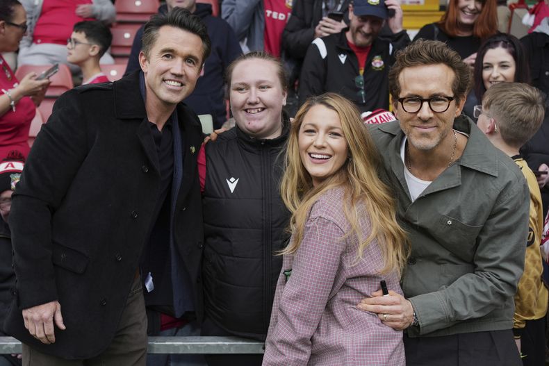 Los codueños de Wrexham Ryan Reynolds (derecha), su esposa Blake Lively (segunda derecha) y Rob McElhenney (izquierda) posan con hinchas previo al partido contra Charlton Athletic, el sábado 26 de abril de 2025, en Wrexham, Gales. (AP Foto/Jon Super)