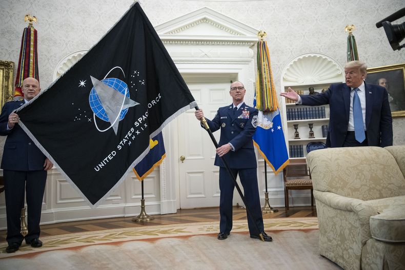 El general John Jay Raymond, comandante del Comando Espacial Estadounidense (izq) y el sargento Roger Towberman (der) sostienen la bandera al lado del presidente Donald Trump durante la presentación de la bandera del Comando Espacial en la Oficina Oval en la Casa Blanca en Washington el 15 de mayo del 2020. (AP foto/Alex Brandon)