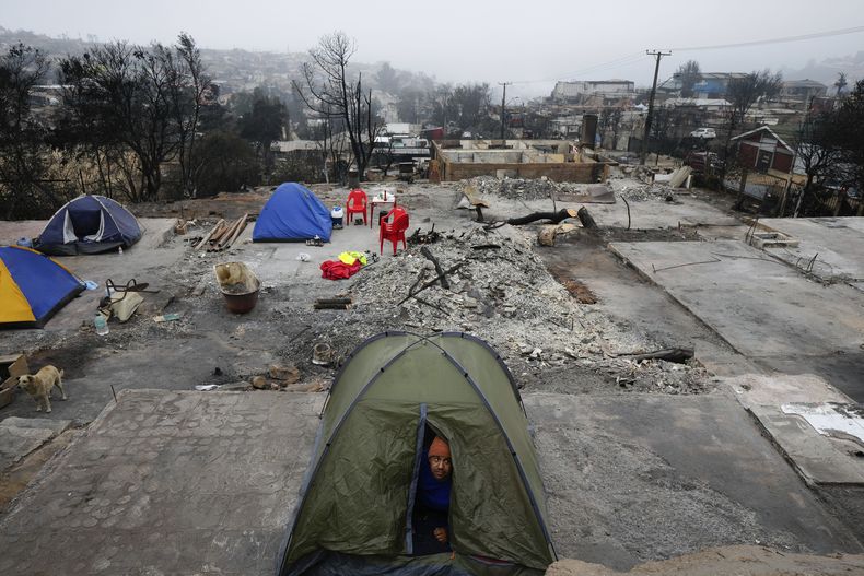 Un hombre mira desde la tienda donde acampó para pasar la noche en el lugar donde se encontraba su casa antes de ser destruida por un incendio forestal en el barrio Villa Independencia de Viña del Mar, Chile, el martes 6 de febrero de 2024. (AP Foto/Esteban Felix)