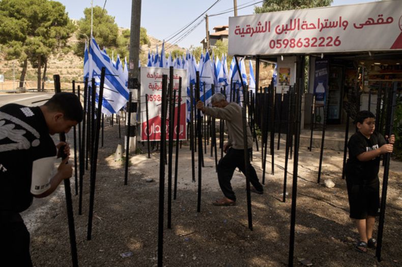 El palestino Mouayad Oweis y sus hijos tratan de retirar astas de bandera colocadas por colonos israelíes para bloquear el acceso a su cafetería en el poblado de al-Lubban al-Sharqiya, Cisjordania, el jueves 8 de octubre de 2026. (AP Foto/Leo Correa)