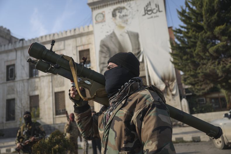 Un combatiente de la oposición siria sostiene un lanzacohetes ante una oficina gubernamental, con la imagen del presidente Bashar Assad con varios balazos en la fachada, tras la toma de Hama por parte de la oposición, en Siria, el 6 de diciembre de 2024. (AP Foto/Ghaith Alsayed)