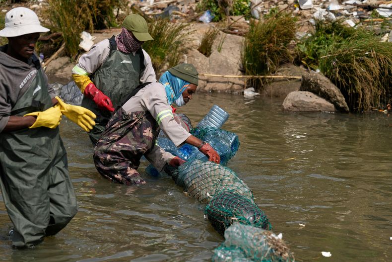 Voluntarios equipados con trajes impermeables desenredan una larga red con basura en el río Jukskei, en la barriada de Alexandra, en Johannesburgo, Sudáfrica, el 12 de noviembre de 2025. (AP Foto/Themba Hadebe)