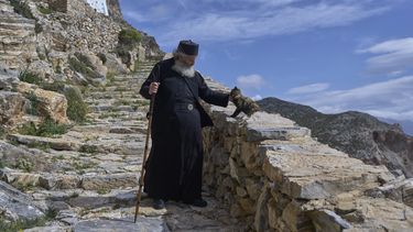 El padre Spyridon de Amorgos, un monje cristiano ortodoxo, acaricia a un gato al salir del monasterio de Panagia Hozoviotissa, en el fondo, en la isla de Amorgos, el domingo 30 de marzo de 2025. (AP Foto/Petros Giannakouris)
