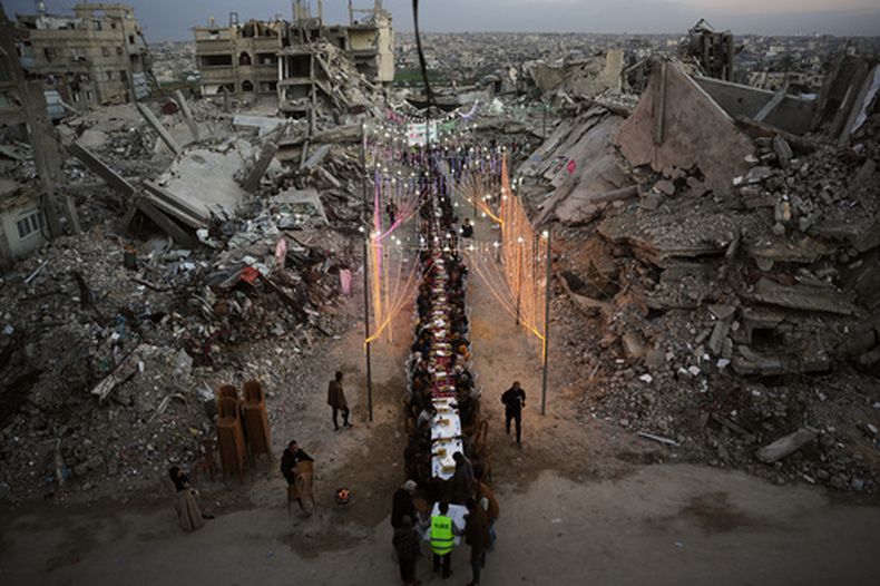 Palestinos sentados en una larga mesa entre los escombros de edificios destruidos mientras rompen el ayuno del Ramadán, el jueves 19 de febrero de 2026, en Jan Yunis, Franja de Gaza. (AP Foto/Abdel Kareem Hana)