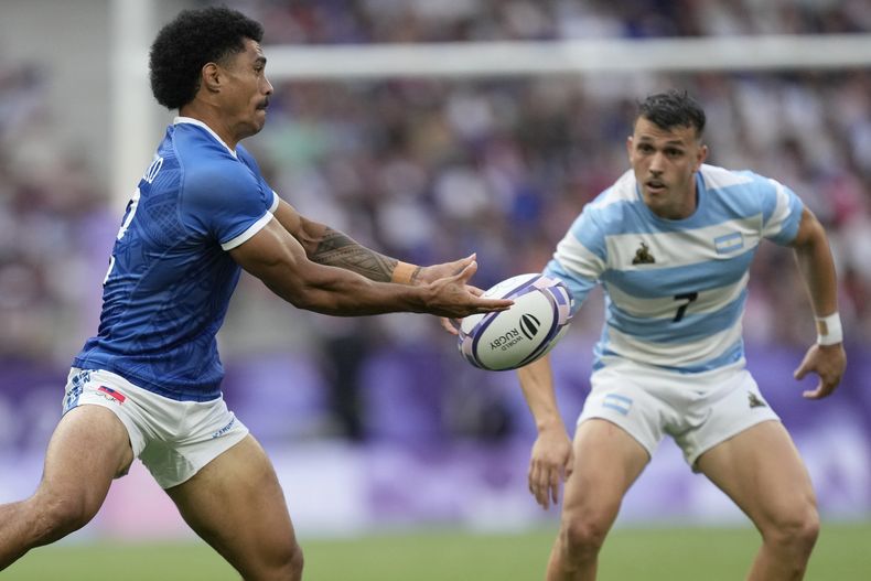 El samoano Vaa Apelu Maliko envía un pase frente a Tobias Wade, de Argentina, durante un partido de rugby 7 en Saint-Denis, el miércoles 24 de julio de 2024(AP Foto/Tsvangirayi Mukwazhi)
