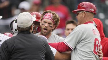 Bryce Harper, centro, de los Filis de Filadelfia, es contenido por el umpire de primera, Ben May, izquierda, y el coach de tercera de los Filis, Dusty Wathan, después de reaccionar a una burla del relevista de los Rockies de Colorado, Jake Bird, en la séptima entrada del juego de béisbol, el domingo 14 de mayo de 2023, en Denver. (AP Foto/David Zalubowski)