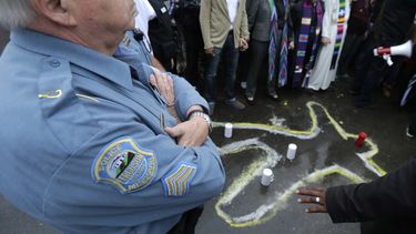 americateve | Un agente de polic&iacute;a de Ferguson, Missouri, permanece de pie en la calle ante la comisar&iacute;a de polic&iacute;a cerca de una silueta dibujada con tiza en recuerdo de Michael Brown, el 13 de octubre de 2014. (Foto AP/Charles Rex Arbogast)