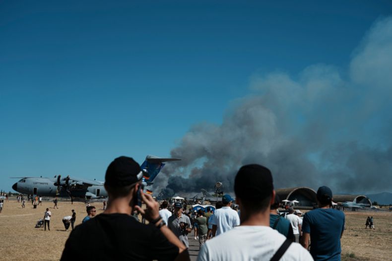 Unas personas observan una columna de humo tras el accidente de un avión militar caza F-4 Phantom de la Fuerza Aérea de Grecia, durante el espectáculo aéreo de la Semana de Vuelo de Atenas en la Base Aérea de Tanagra, al norte de Atenas, el sábado 5 de septiembre de 2026. (Foto AP/Kallista Allaway)