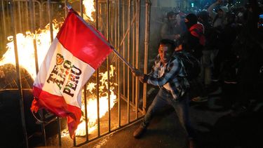 Un manifestante ondea una bandera peruana mientras una muñeca de cartón arde frente al Congreso durante una protesta contra el nuevo presidente José Jeri en Lima, Perú, el miércoles 15 de octubre de 2025. (AP Foto/Martín Mejía)