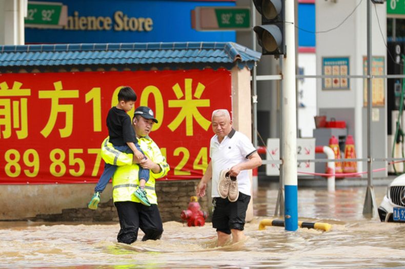 En esta imagen publicada por la agencia de noticias Xinhua, un policía sostiene a un niño mientras vadea una calle inundada en la ciudad de Duyn, en la provincia suroccidental china de Guizhou, el martes 19 de mayo de 2026. (Xiao Wei/Xinhua via AP)