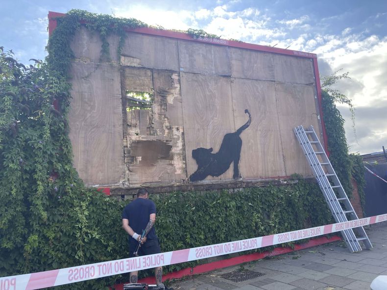 Contratistas comienzan a desmantelar una mampara con una nueva obra de arte de Banksy que representa un felino estirándose en Cricklewood, noroeste de Londres, el sábado 10 de agosto de 2024. (Jordan Reynolds/PA via AP)
