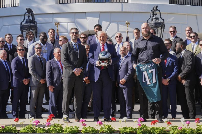 El tackle ofensivo de los Eagles de Filadelfia Lane Johnson junto al entrenador Nick Sirianni y al presidente de los Estados Unidos, quien sostiene un casco durante la visita de los campeones defensores del Super Bowl a la Casa Blanca el lunes 28 de abril del 2025. (AP Foto/Mark Schiefelbein)