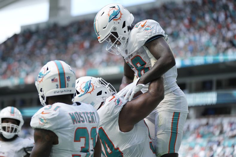 El defensive tackle Christian Wilkins (94), levanta a su compañero de los Dolphins de Miami DeVon Achane (28) después de que anotó un touchdown en la segunda mitad del partido ante los Broncos de Denver, el domingo 24 de septiembre de 2023, en Miami Gardens, Florida. (AP Foto/Rebecca Blackwell)