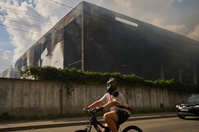 Un residente pasa en bici, con el rostro cubierto con una máscara de gas, por delante de un almacén parcialmente destruido por un ataque con drones rusos, en Brovary, a las afueras de Kiev, el 4 de septiembre de 2026. (AP Foto/Francisco Seco)
