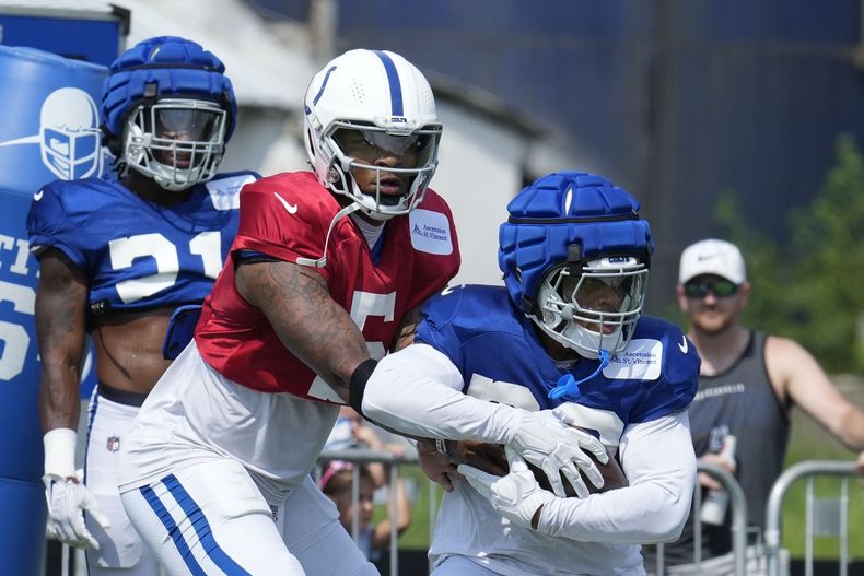 Anthony Richardson, centro, quarterback de los Colts de Indianápolis, le entrega el balón al running back Jonathan Taylor, derecha, durante el campo de entrenamiento del equipo de la NFL, el domingo 4 de agosto de 2024, en Westfield, Indiana. (AP Foto/Darron Cummings)