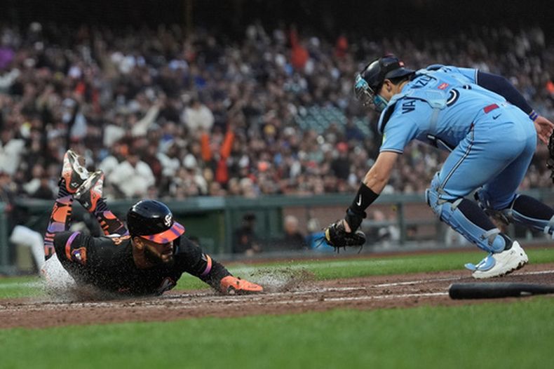 Heliot Ramos (izquierda), de los Gigantes de San Francisco, se desliza en el plato para anotar contra el receptor de los Azulejos de Toronto, Brandon Valenzuela, durante la quinta entrada de un partido de béisbol, el martes 7 de julio de 2026, en San Francisco. (Foto AP/Jeff Chiu)