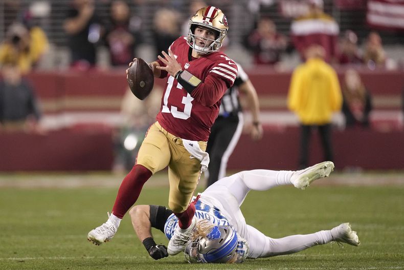 El quarterback Brock Purdy (13), de los 49ers de San Francisco, corre en contra de los Lions de Detroit, superando al linebacker Alex Anzalone, durante la segunda mitad del Juego de Campeonato de la NFC, en Santa Clara, California, el domingo 18 de enero de 2024. (AP Foto/Mark J. Terrill)