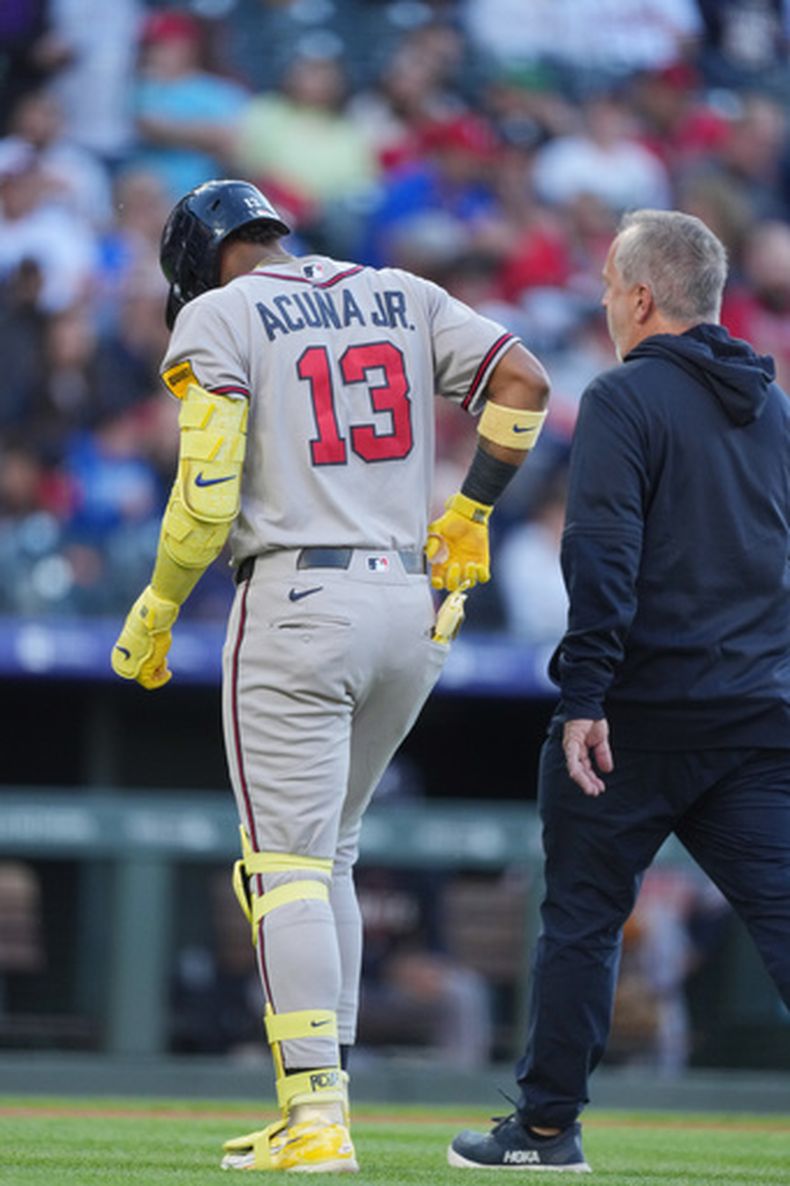 Ronald Acuña Jr. (13), de los Bravos de Atlanta, es acompañado rumbo al dugout después de sufrir una lesión en la segunda entrada del juego de béisbol de Grandes Ligas contra los Rockies de Colorado, el sábado 2 de mayo de 2026, en Denver. (AP Foto/David Zalubowski)
