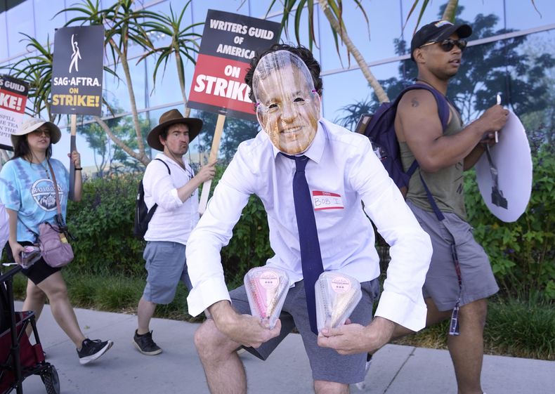 El miembro del sindicato SAG-AFTRA, Gregory Lay, propietario de la tienda East Side Cheesecakes, con una máscara del director general de Disney, Bob Iger, reparte rebanadas de pastel a los trabajadores en una protesta frente a los estudios de Netflix el martes 18 de julio de 2023 en Los Ángeles. (Foto AP/Chris Pizzello)