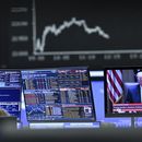 Tras una pantalla que muestra al presidente de Estados Unidos, Donald Trump, la pantalla con el índice bursátil Dax muestra un precio a la baja de las acciones en Fráncfort, Alemania, el jueves 3 de abril de 2025, después de Trump presentara un paquete de aranceles que llevó las bolsas a pérdidas. (Arne Dedert/dpa via AP)