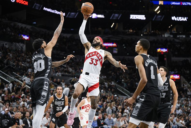Gary Trent Jr. (33), de los Raptors de Toronto, dispara ante la presión defensiva de Julian Champagnie (30) y la mirada de Victor Wembanyama (1), de los Spurs de San Antonio, durante la segunda mitad del juego de baloncesto de la NBA, el domingo 5 de noviembre de 2023, en San Antonio. (AP Foto/Darren Abate)