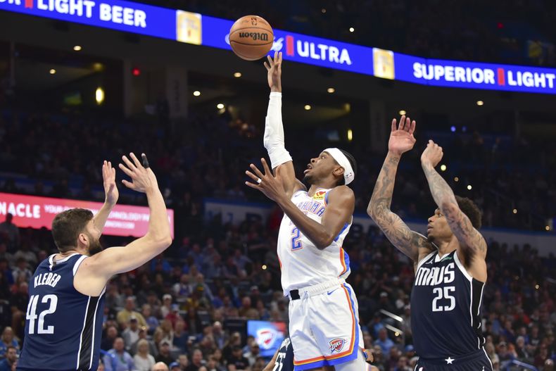 El base del Thunder de Oklahoma City Shai Gilgeous-Alexander lanza el balón entre los aleros de los Mavericks de Dallas Maxi Kleber y P.J. Washington en el encuentro de la NBA del jueves 14 de marzo del 2024. (AP Foto/Kyle Phillips)