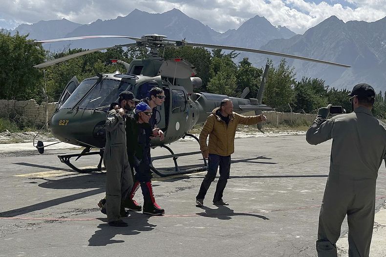 Dos alpinistas rusos, al centro, evacuados del campamento de base de una de las montañas más altas de Pakistán una semana después de quedar varados en un remoto pico tras ser alcanzados por una formación de hielo, reciben ayuda de un voluntario al llegar a Skardu, Pakistán, el jueves 22 de agosto de 2024. (AP Foto/M.H. Balti)