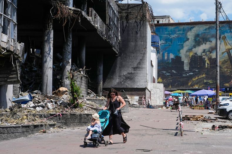 Una madre camina con su bebé en carriola junto a un edificio dañado cubierto de pinturas de artistas callejeros y un gran mercado urbano que fue destruido recientemente por misiles rusos en Kiev, Ucrania, el lunes 22 de junio de 2026. (Foto AP/Efrem Lukatsky)