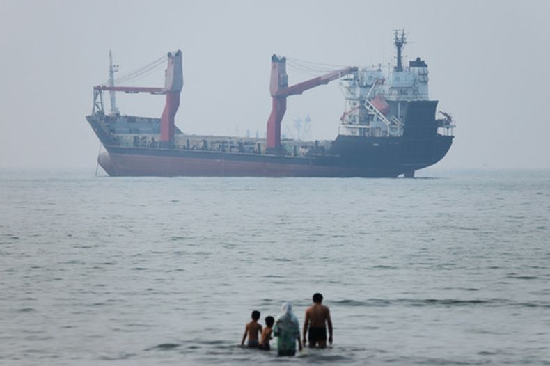 Varias personas se meten en el agua en la orilla mientras un carguero aparece fondeado en el estrecho de Ormuz, ante la costa de Bandar Abbas, Irán, el 30 de junio de 2026. (Amirhosein Khorgooi/ISNA via AP)