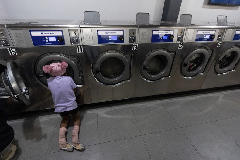 Maickeliys Rodriguez, de 6 años, de Venezuela, mira la colada de su familia dando vueltas en una máquina de una lavandería cerca del refugio de migrantes donde se alojan en Tijuana, México, el viernes 31 de enero de 2025. (AP Foto/Gregory Bull)