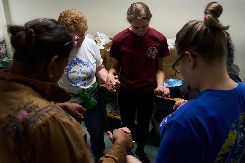 Feligreses del Santuario del Sagrado Corazón y voluntarios rezan en el sótano de una iglesia antes de entregar alimentos donados a familias que temen salir de sus hogares para ir al supermercado debido a las redadas de inmigración, el 11 de octubre de 2025, en Washington. (AP Foto/Luis Andrés Henao)