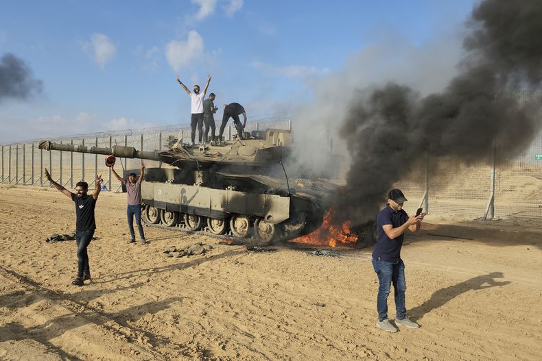 Palestinos festejan al lado de un tanque israelí destruido en una valla en la Franja de Gaza, al este de Khan Younis, el sábado 7 de octubre de 2023. (AP Foto)