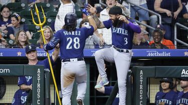 El venezolano Eugenio Suárez de los Marineros de Seattle sostiene un tridente mientras celebra con J.P. Crawford su segundo jonrón de la noche en la novena entrada ante los Astros de Houston el jueves 6 de julio del 2023. (AP Foto/Michael Wyke)