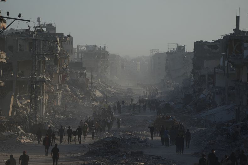 Palestinos desplazados cargan con sus pertenencias mientras caminan entre los dañados edificios de la calle Al-Jalaa, en la Ciudad de Gaza, el 11 de octubre de 2025, luego de que Israel y Hamás acordaron una pausa en la guerra y la liberación de los rehenes. (AP Foto/Abdel Kareem Hana)