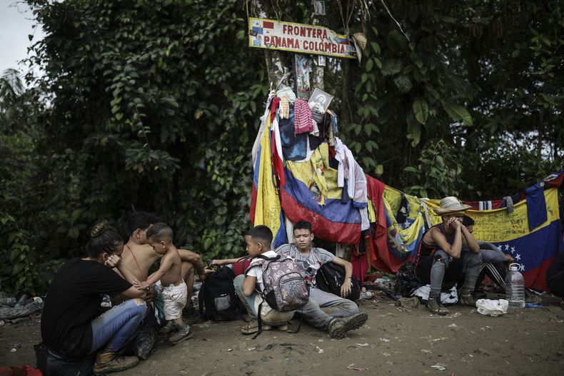 ARCHIVO - Migrantes sentados bajo un cartel que marca la frontera entre Panamá y Colombia durante su viaje a través del Tapón del Darién, el 9 de mayo de 2023. Abrumado por el resurgimiento de migrantes que cruzan la selva del Darién en la frontera con Colombia, el gobierno de Panamá anunció el jueves 24 de agosto de 2023 que tomará medidas concretas. (AP Foto/Iván Valencia, Archivo)