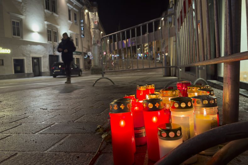 Un peatón camina junto a unas velas en el lugar de un ataque con arma blanca en Villach, Austria, el domingo 16 de febrero de 2025. (AP foto/Darko Bandic)