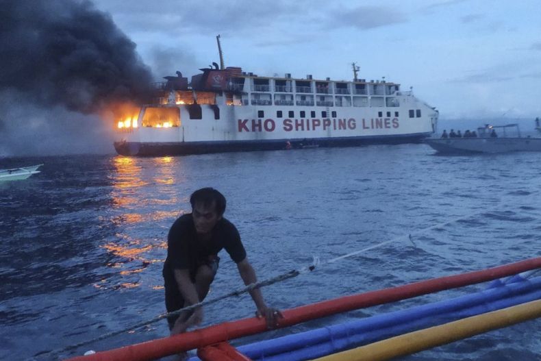 En una imagen proporcionada por la guardia costera de Filipinas, un hombre empuja un bote cerca del ferry filipino M/V Esperanza Star que se incendia en aguas frente a Panglao, en la provincia Bohol, Filiínas, el domingo 18 de junio de 2023. (Guardia Costera de Filipinas vía AP)