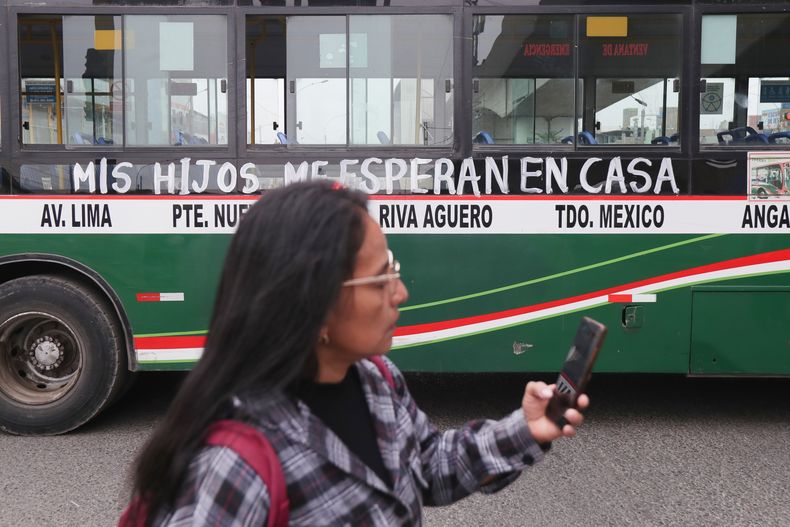 Una mujer pasa junto a un autobús con la leyenda Mis hijos me esperan en casa durante una huelga en contra de las extorsiones a transportistas en las afueras de Lima, Perú, el lunes 6 de octubre de 2025. (AP Foto/Jao Yamunaque)