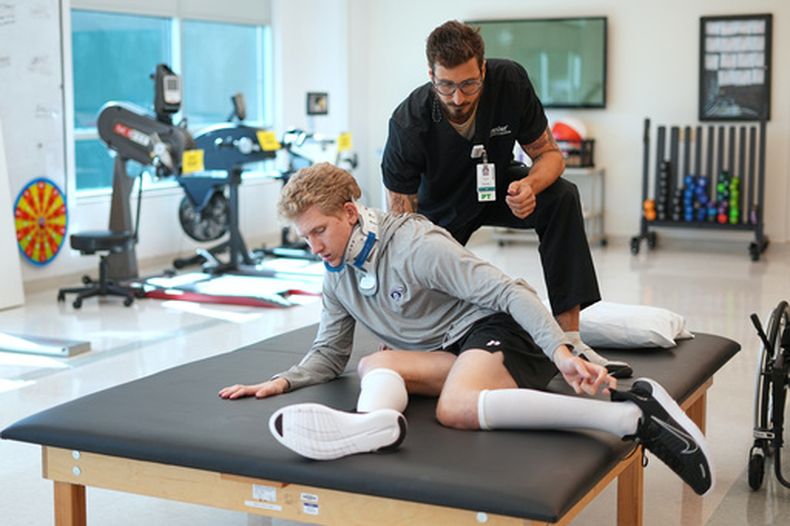 Ryan Lasko, prospecto de ligas menores de los Atléticos, recibe ayuda del fisioterapeuta Daniel Gabrielli el martes 15 de septiembre de 2026, para rehabilitarse tras una lesión grave de columna vertebral (AP Foto/Matt Rourke)
