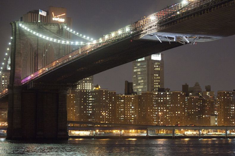 Láminas cuelgan del Puente de Brooklyn después de que una grúa que era transportada en un barco chocó contra la parte inferior del puente, el lunes 13 de marzo de 2012, en Nueva York. (AP Foto/John Minchillo, Archivo)